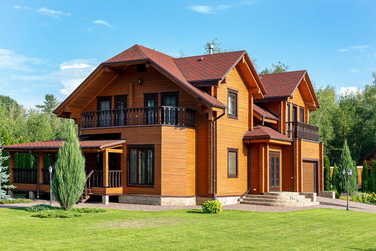 Beautiful luxury big wooden house. Timber cottage villa with with green lawn, garden and blue sky on background.